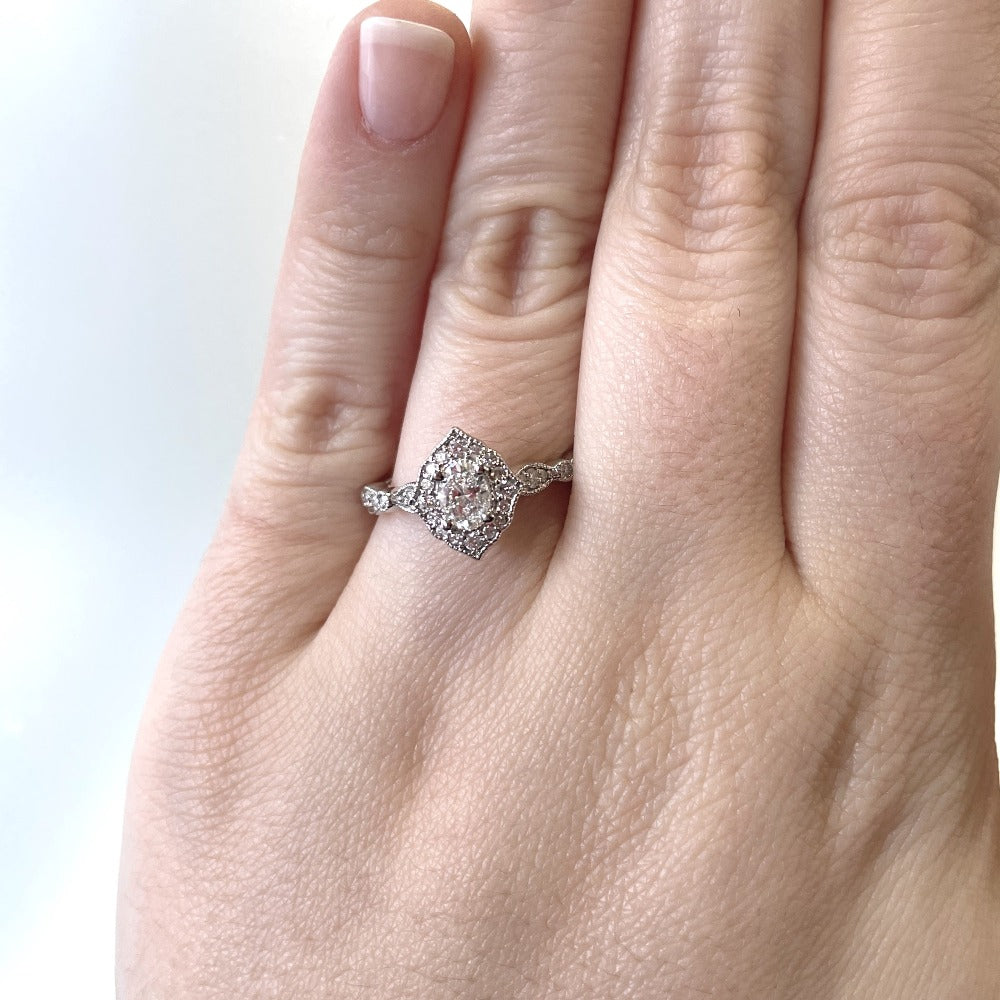 up close detail view of 14kw oval center halo style vintage inspired engagement ring on models hand.